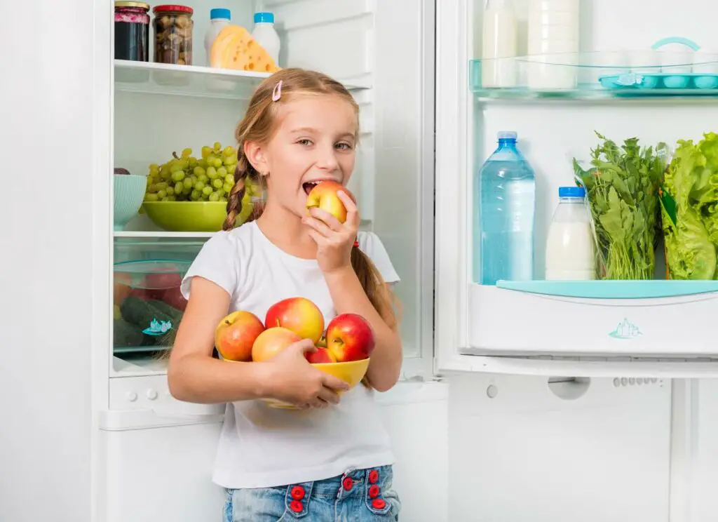 small girl taking apple from refrigerator